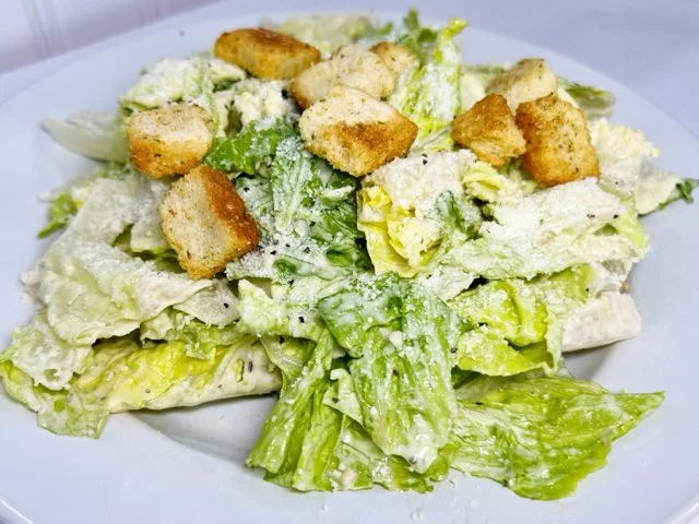 A fresh Caesar salad featuring crisp romaine lettuce, grated cheese, and crunchy croutons served on a white plate.