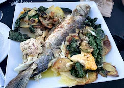 A whole fish is plated with a variety of roasted vegetables, including potatoes, cauliflower, and leafy greens.