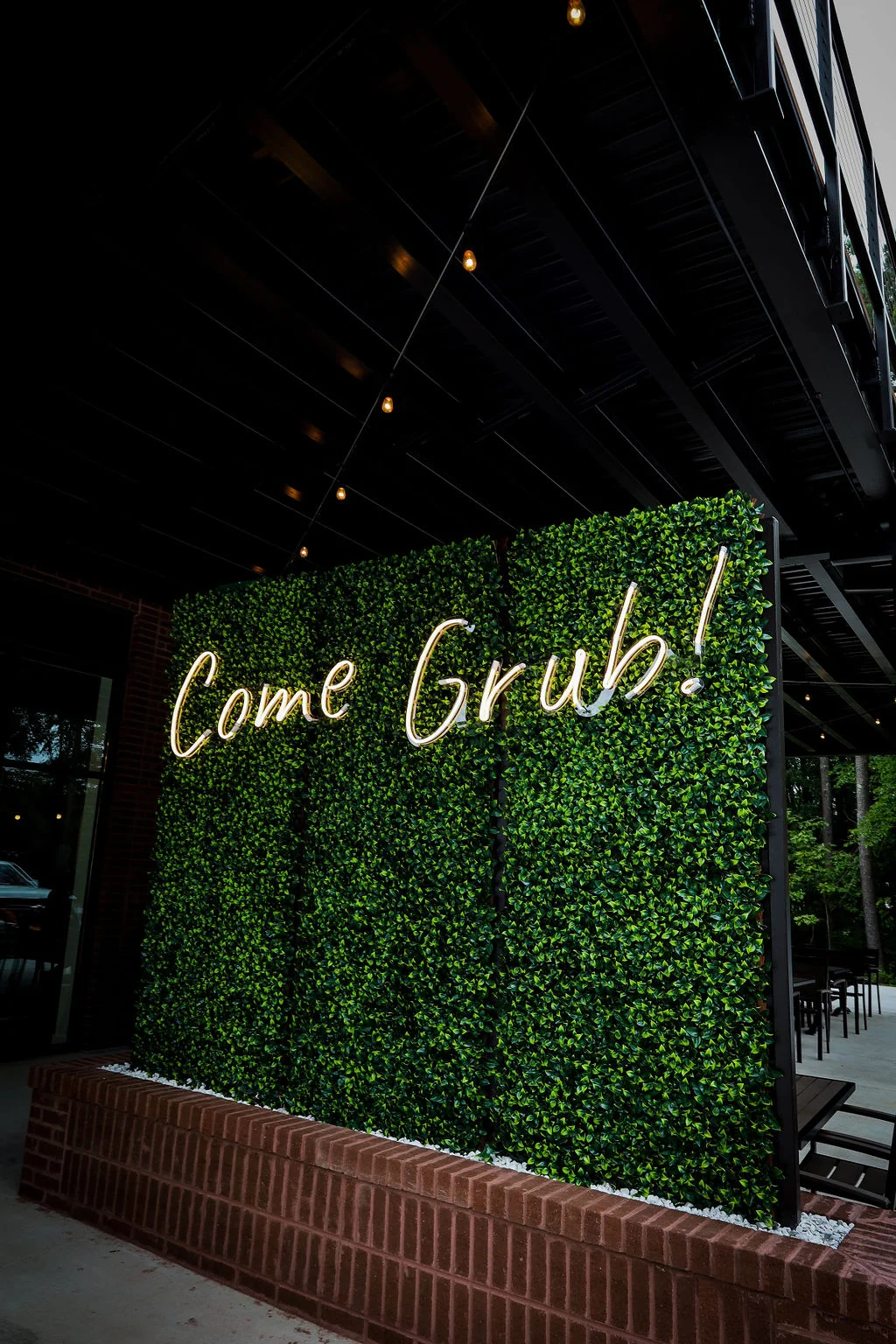 Restaurant exterior with greenery and neon sign inviting guests to dine