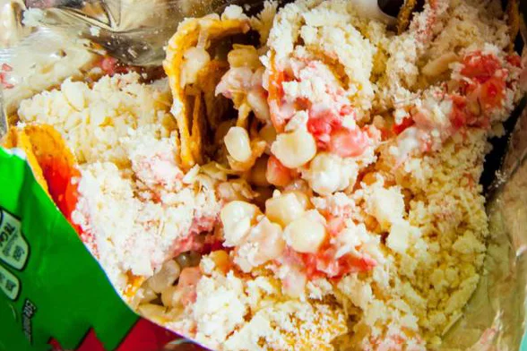 A close-up view of a messy dish featuring broken tortilla chips mixed with various toppings like cheese and corn.