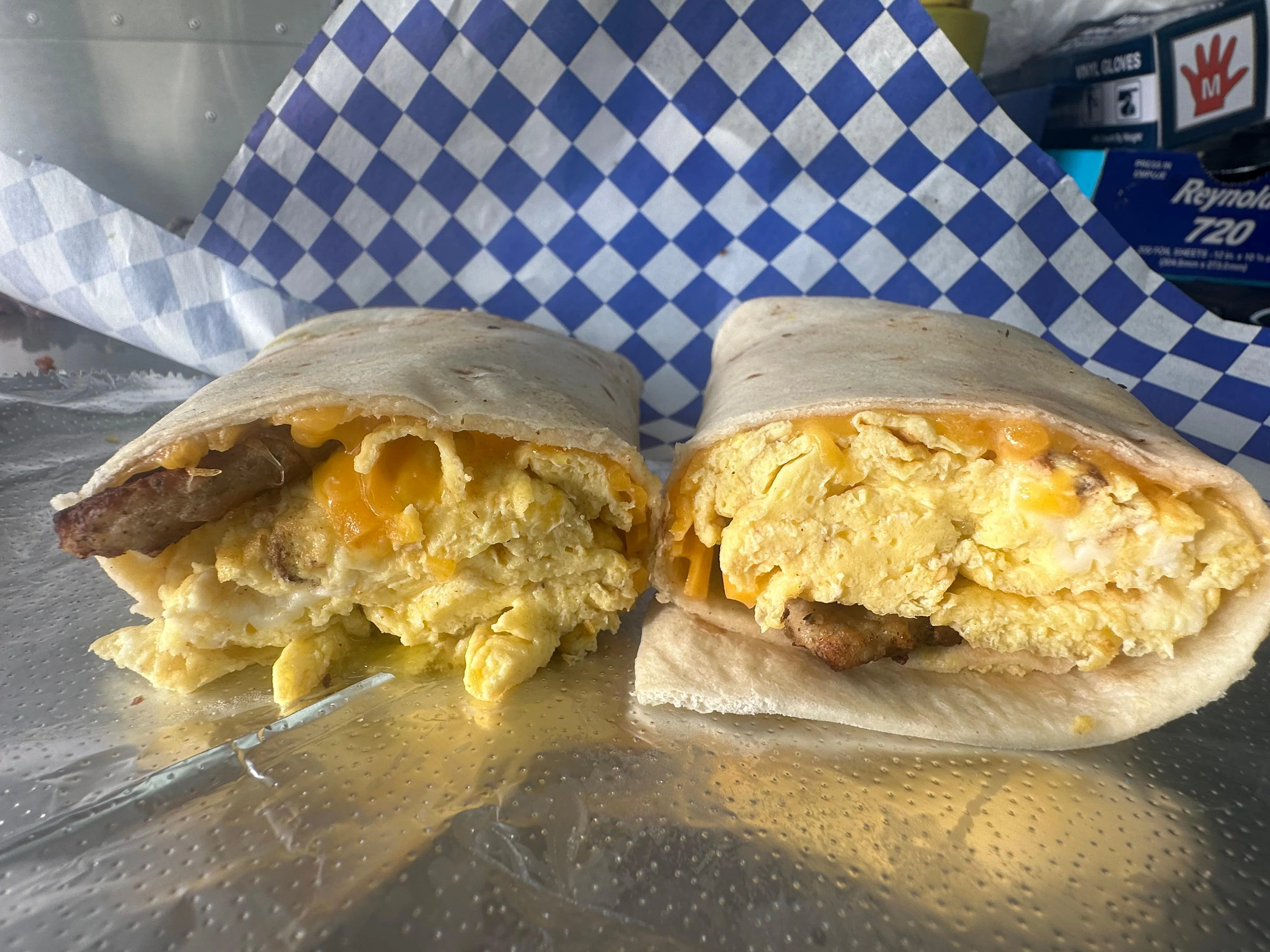 Two breakfast burritos filled with scrambled eggs, cheese, and sausage, served on a checkered paper.