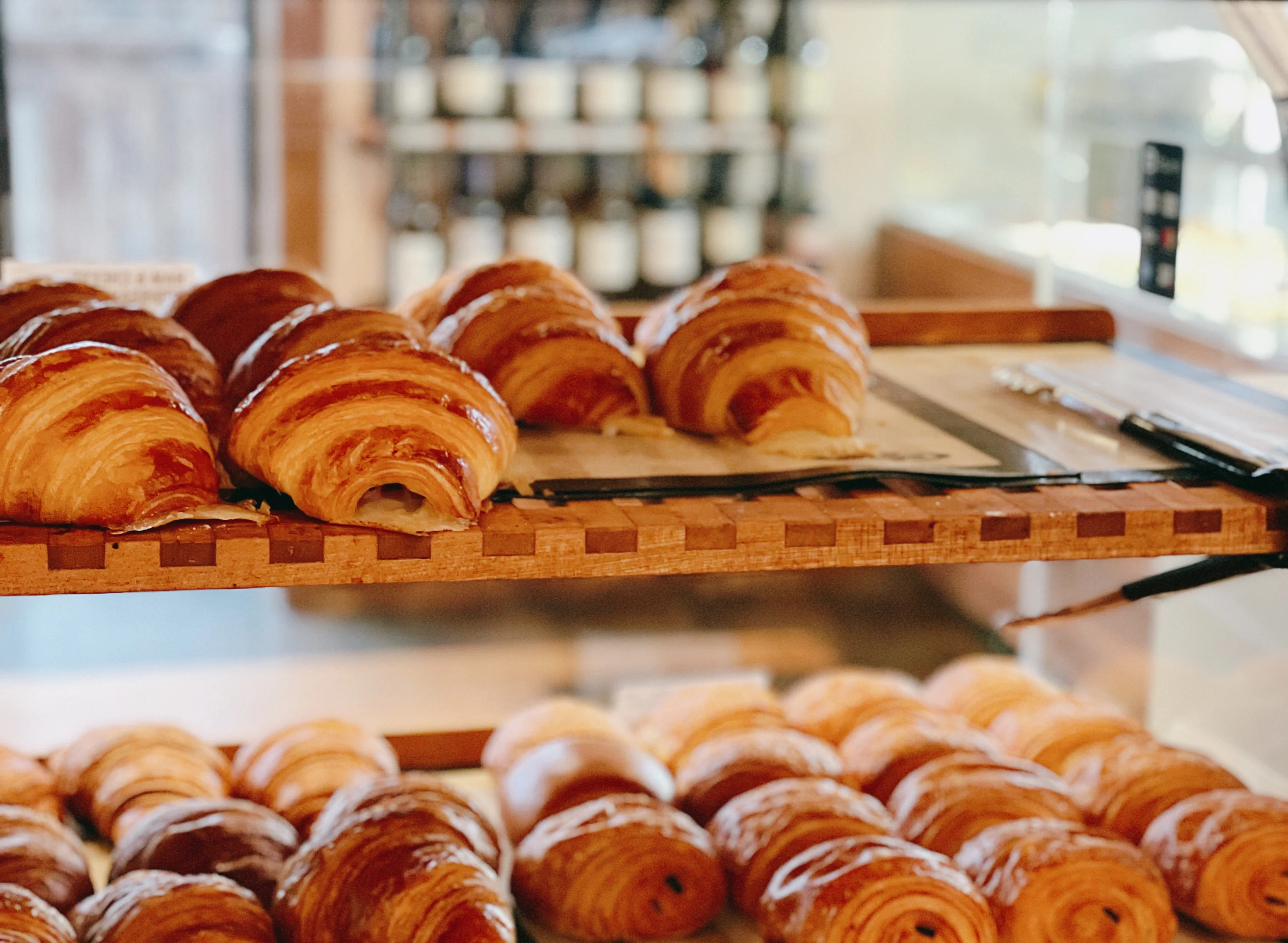 Golden croissants in a bakery display case at La Boulangerie & Co, Logan Square location. Freshly baked daily with French flour and real butter.