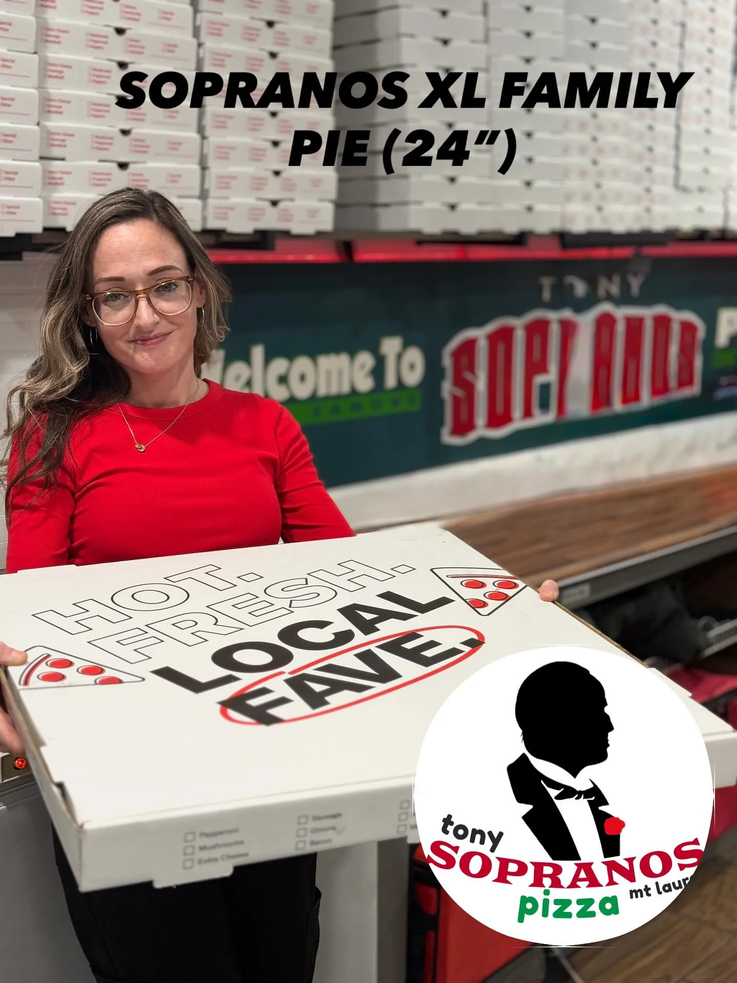 A woman holding a large pizza box that says 'HOT. FRESH. LOCAL FAVE' against a backdrop of stacked pizza boxes.