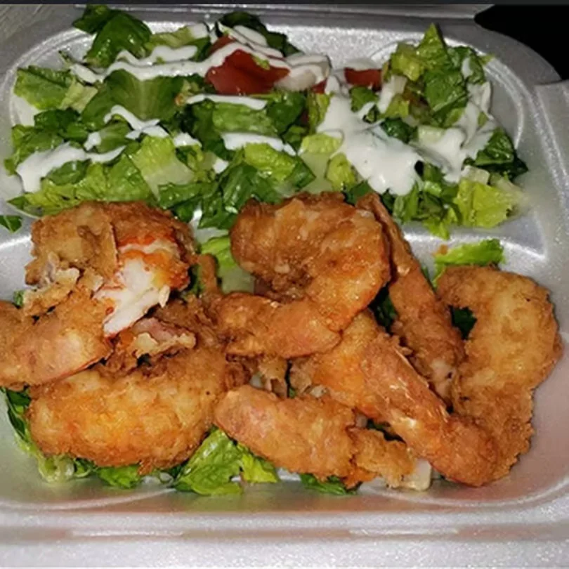 Fried shrimp served on lettuce with a side salad and dressing.