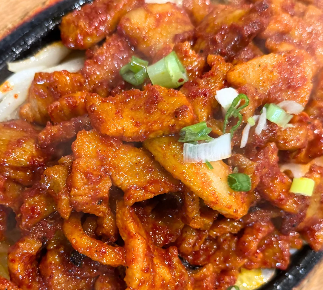 Sizzling spicy chicken dish topped with green onions on a hot plate.