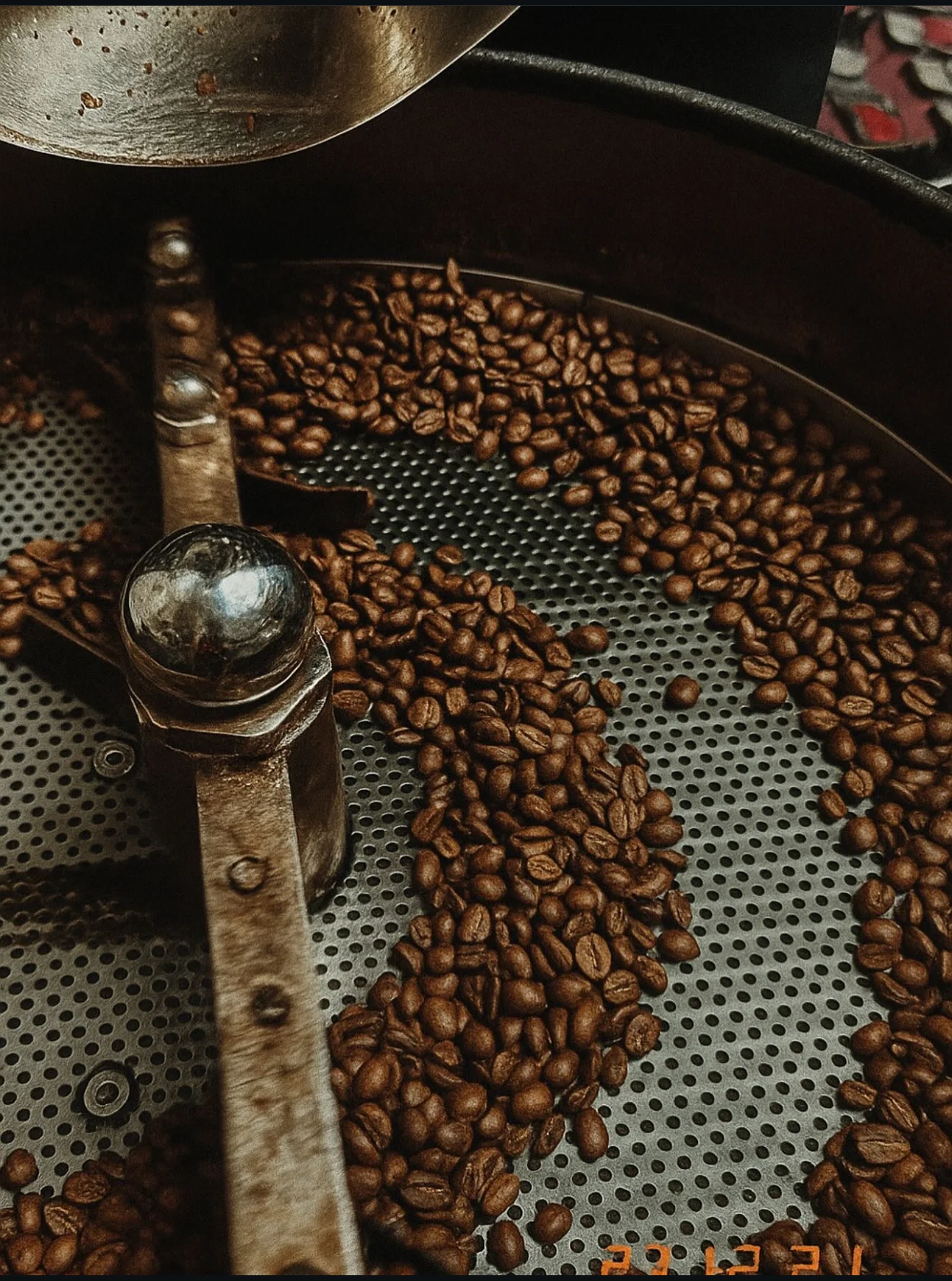 Close-up of roasted coffee beans in a roasting machine, with a metallic scoop overseeing the process.