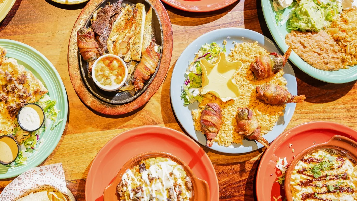 Overhead spread of Mexican fajitas, rice, beans, enchiladas, and bacon-wrapped shrimp