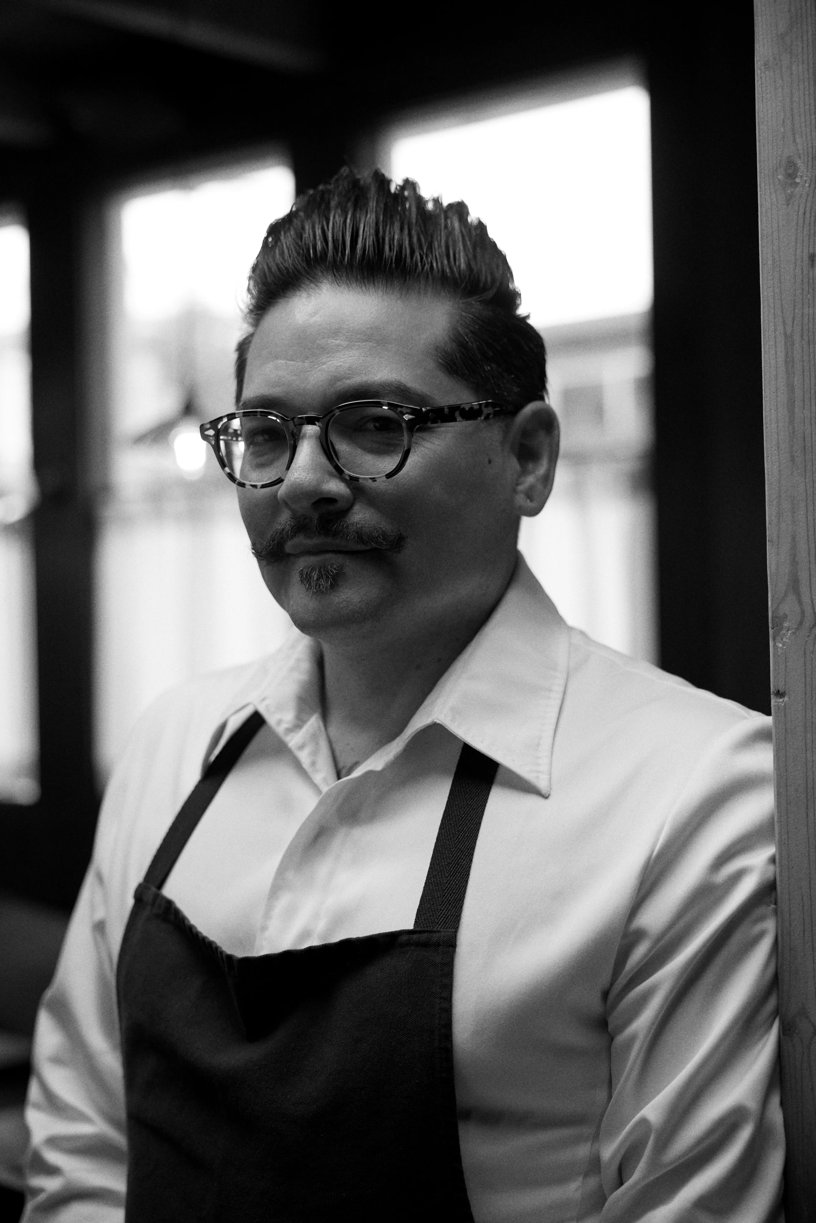 Chef in a white shirt and apron posing in a restaurant setting
