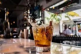 A glass of whiskey with ice splashing on a bar counter.
