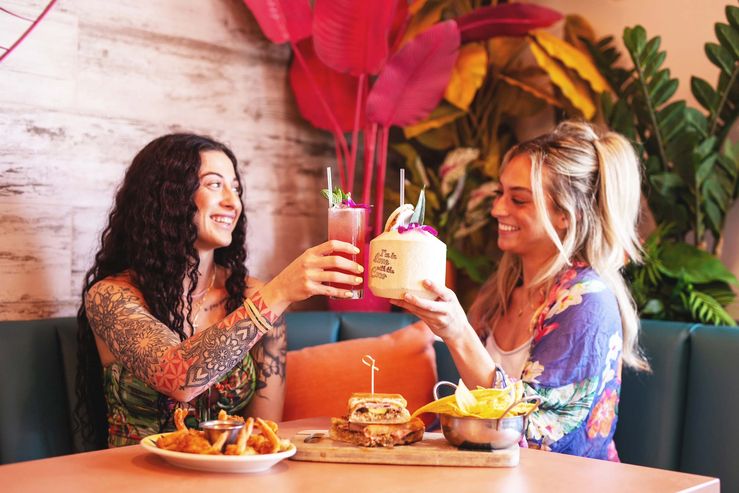 Two friends toasting tropical cocktails in a vibrant restaurant setting