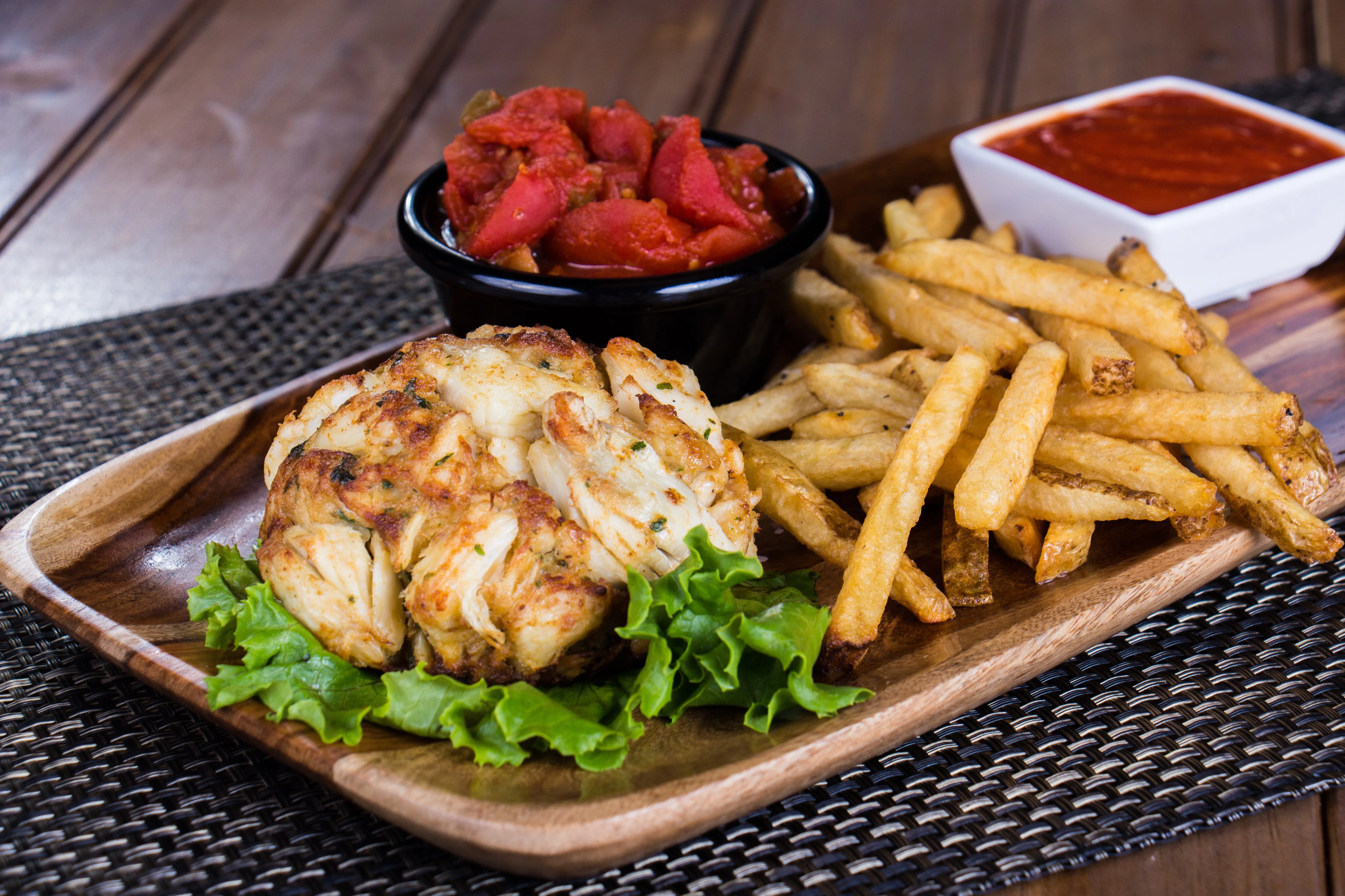 Crab cake with fries and salsa, served on a wooden platter