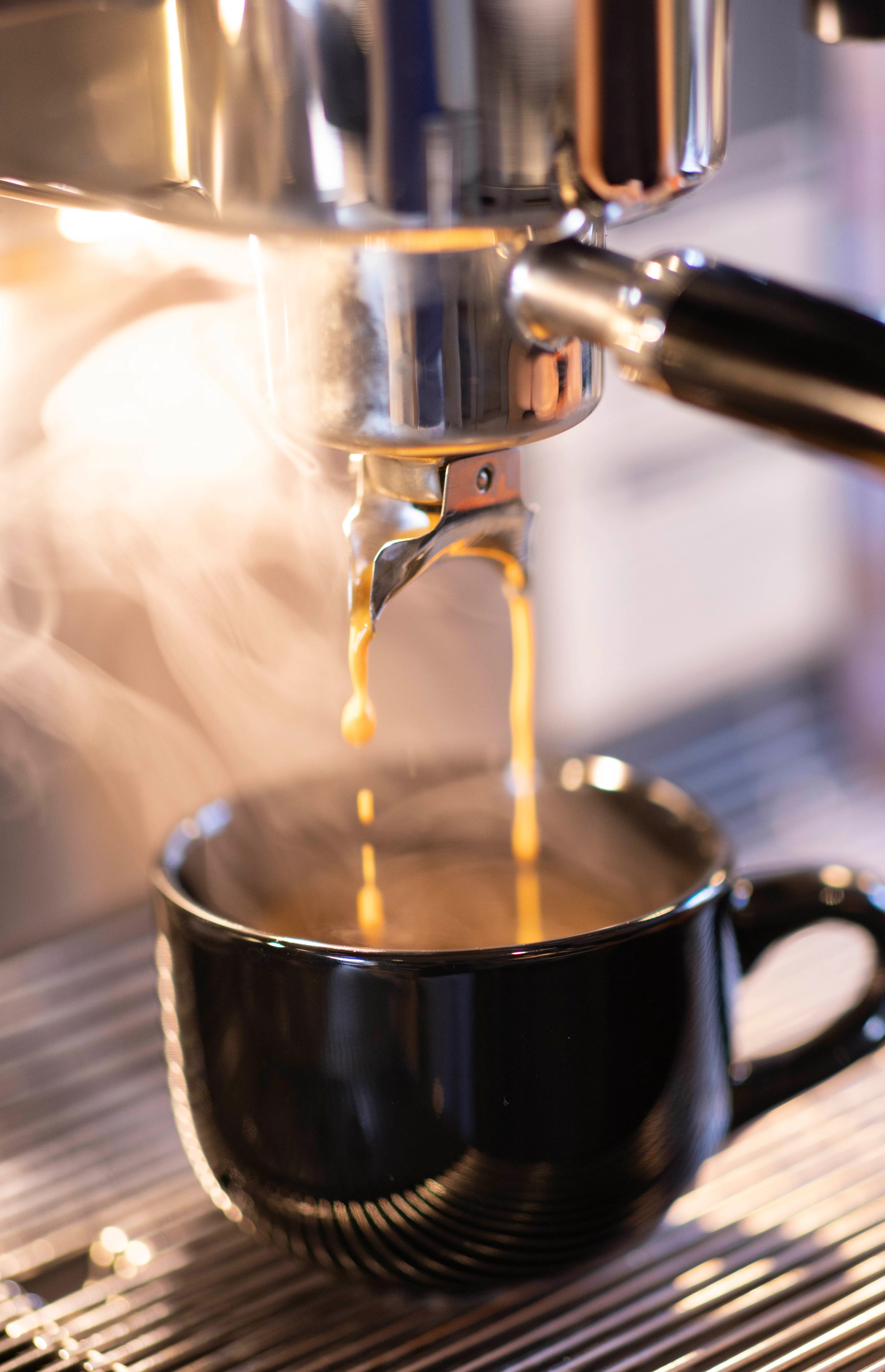 Espresso pouring into a black cup with steam rising