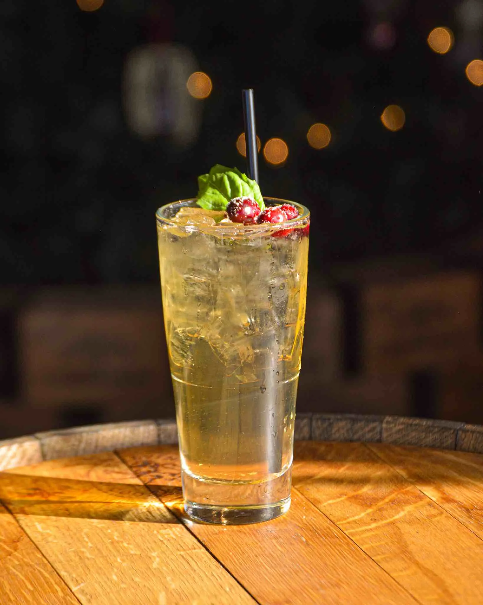 Partridge in a Pear Tree cocktail sitting on a barrel with Christmas lights in the background