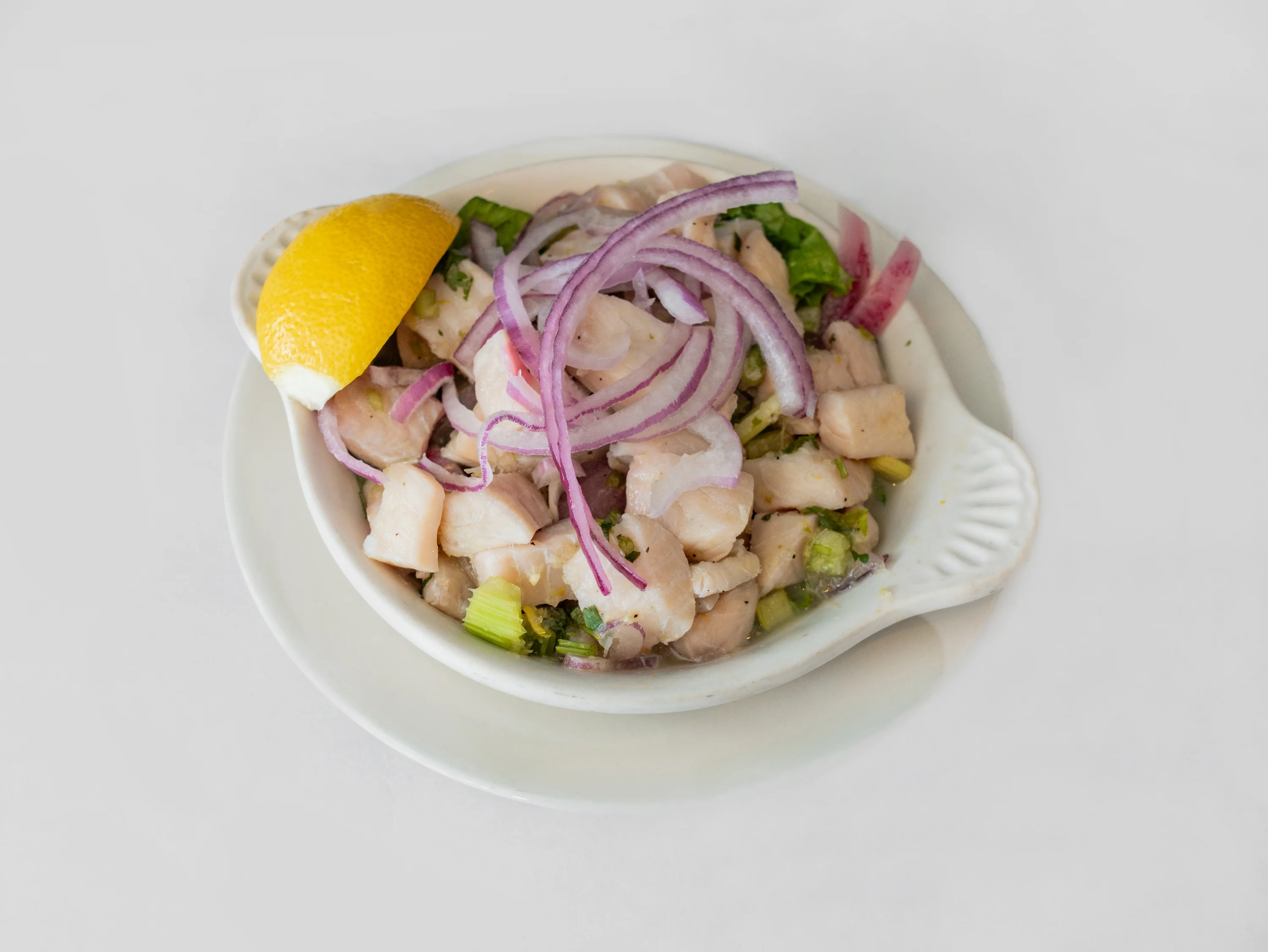 A bowl of ceviche, featuring diced fish, red onions, and chopped vegetables, garnished with a slice of lemon.