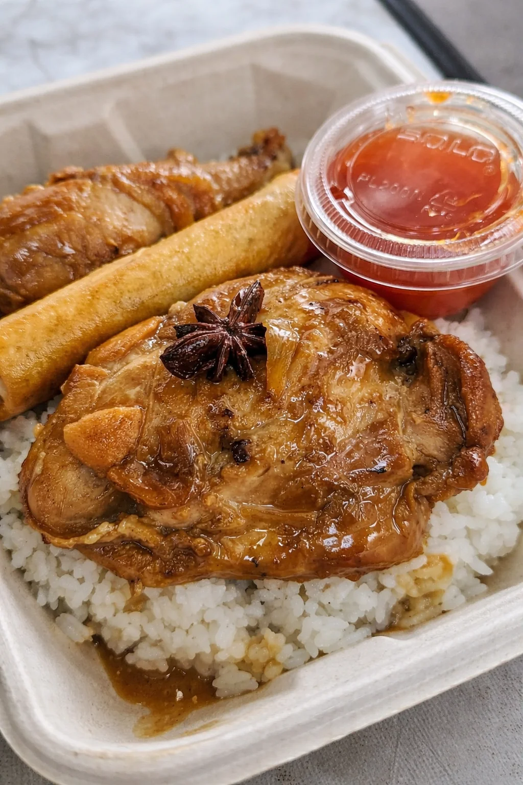 A meal featuring chicken thighs with sweet sauce, accompanied by rice, a spring roll, and a cup of dipping sauce.