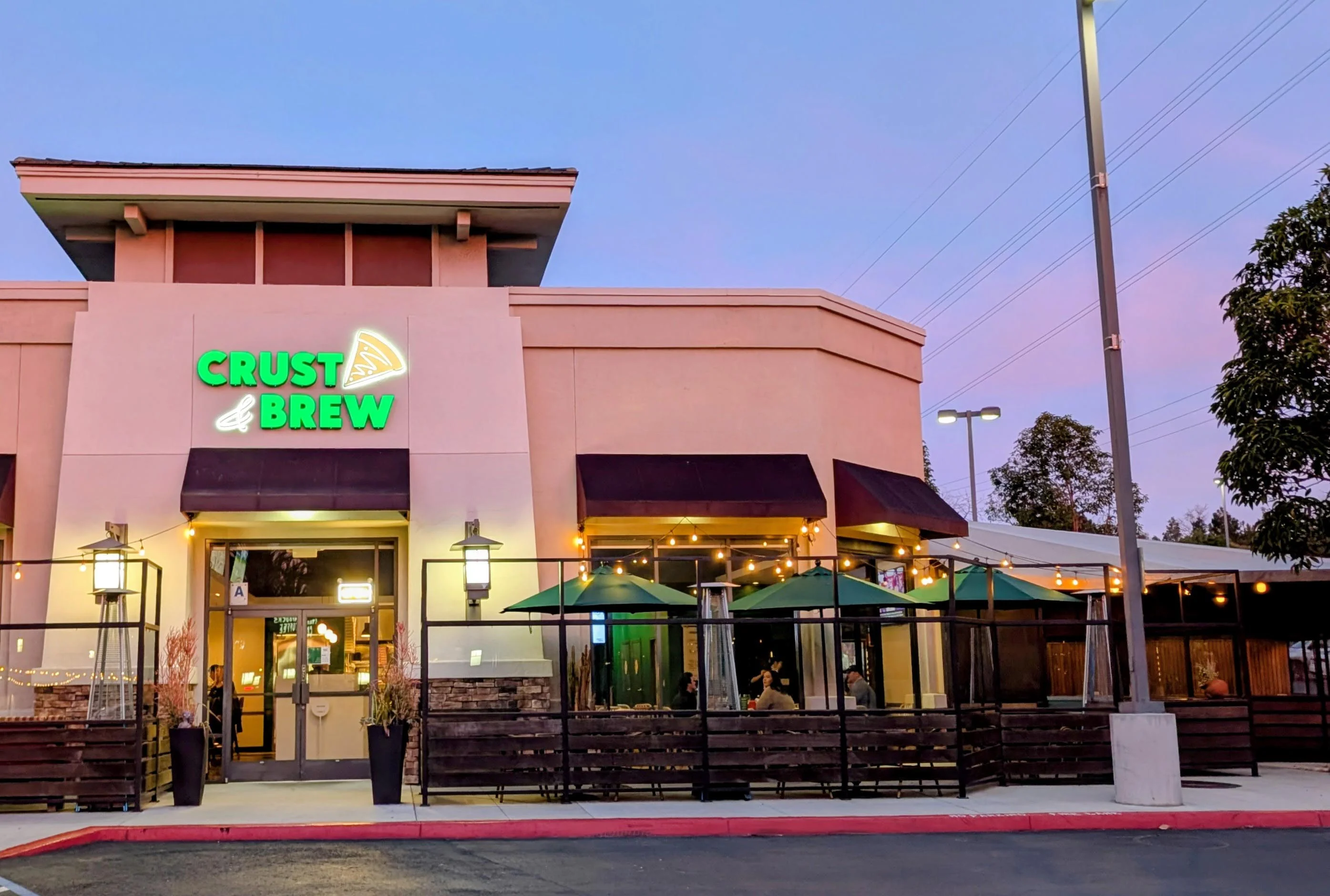 The outside of a restaurant with a front patio and a sign that says 'CRUST & BREW.'