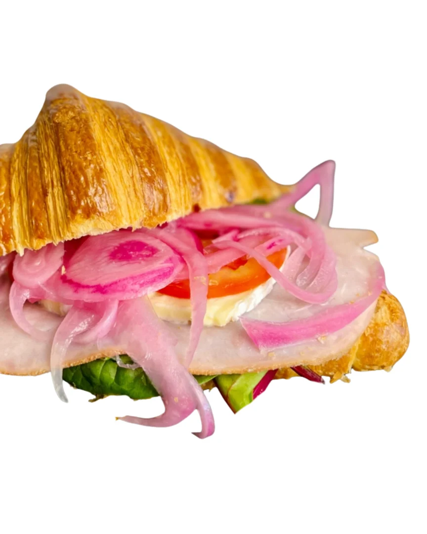 A croissant sandwich filled with layers of ham, onions, tomato, and lettuce.
