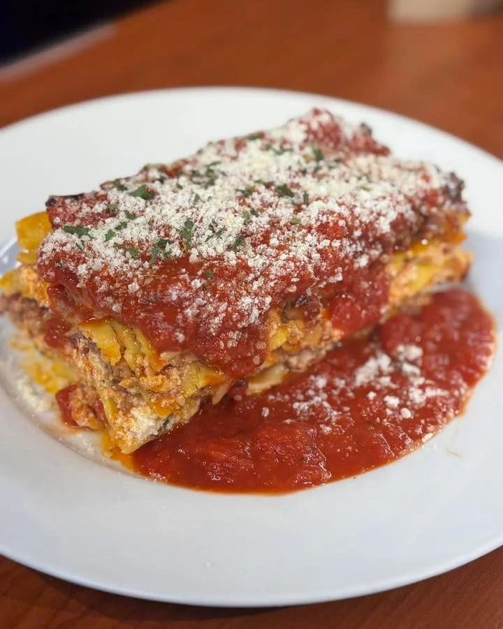 A serving of lasagna topped with marinara sauce and cheese, placed on a white plate.