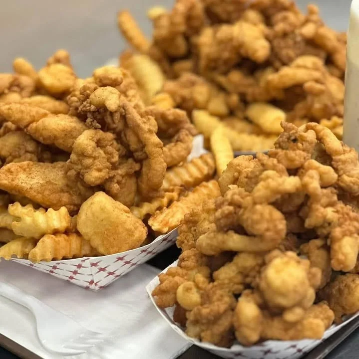 A serving of crispy fried chicken pieces piled on a plate, accompanied by crinkle-cut fries.