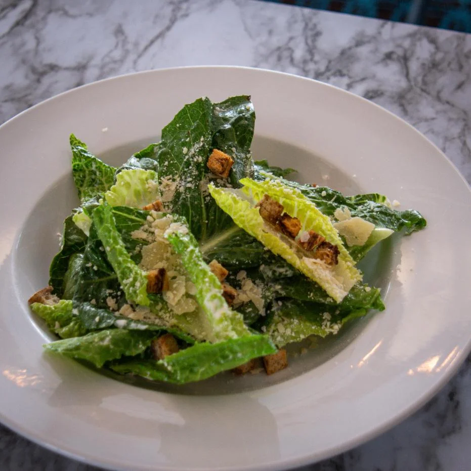 A classic Caesar salad with romaine lettuce, croutons, and sprinkled with cheese. The ingredients are elegantly arranged on a white plate.