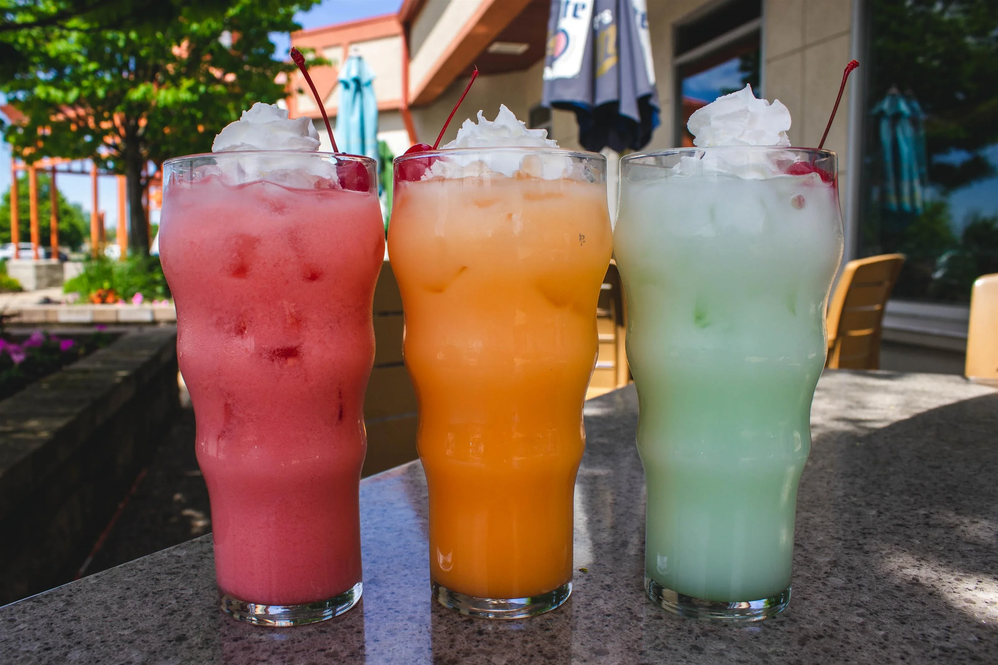Colorful tropical mocktails with whipped cream and cherries on a sunny patio