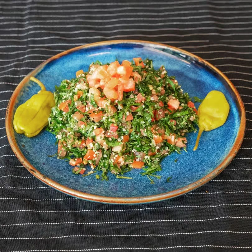 Fresh tabbouleh salad with tomatoes and green peppers on a blue plate.