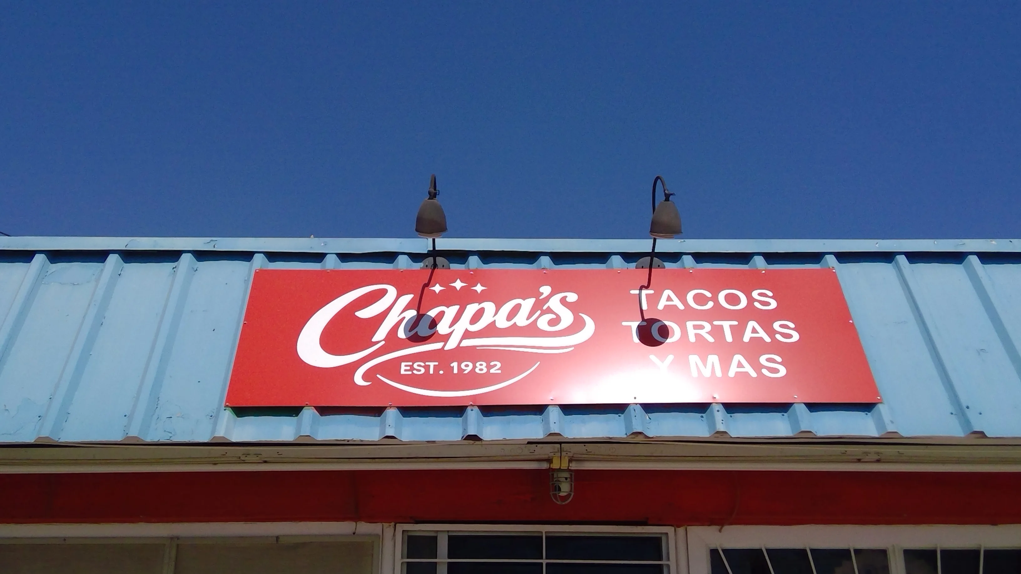 A restaurant sign displaying the name and offerings of the establishment, which specializes in tacos and tortas. The sign is bright red with white lettering.