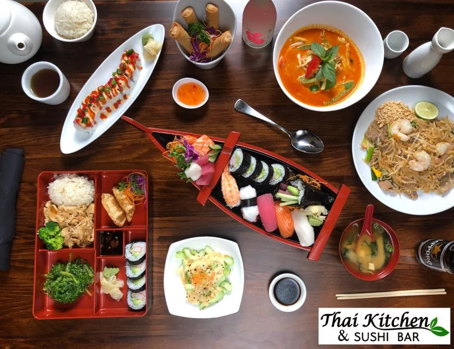 Assorted Thai dishes including sushi and pad thai on a wooden table