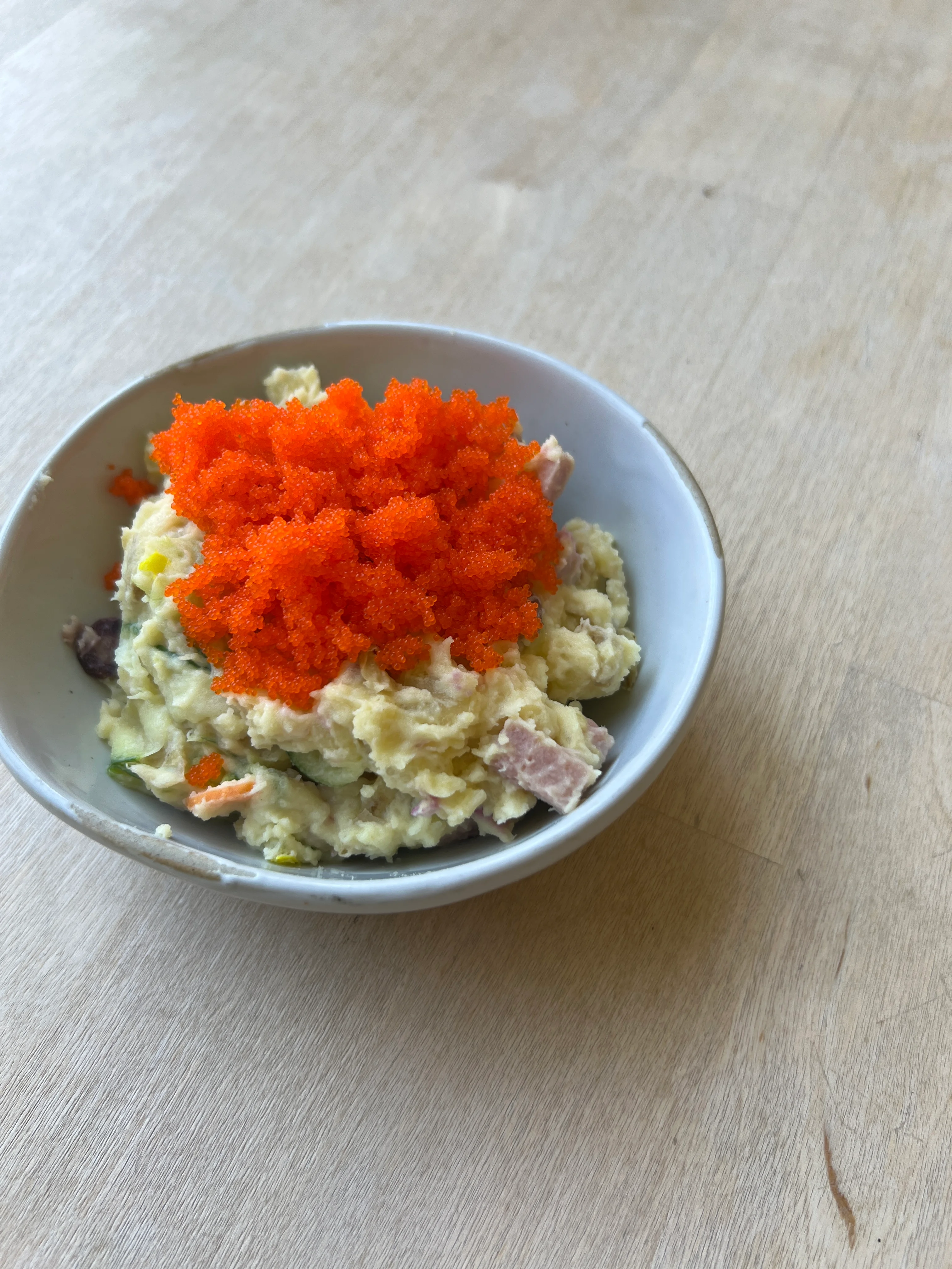 A bowl filled with a creamy dish topped with bright orange fish roe, placed on a wooden surface.
