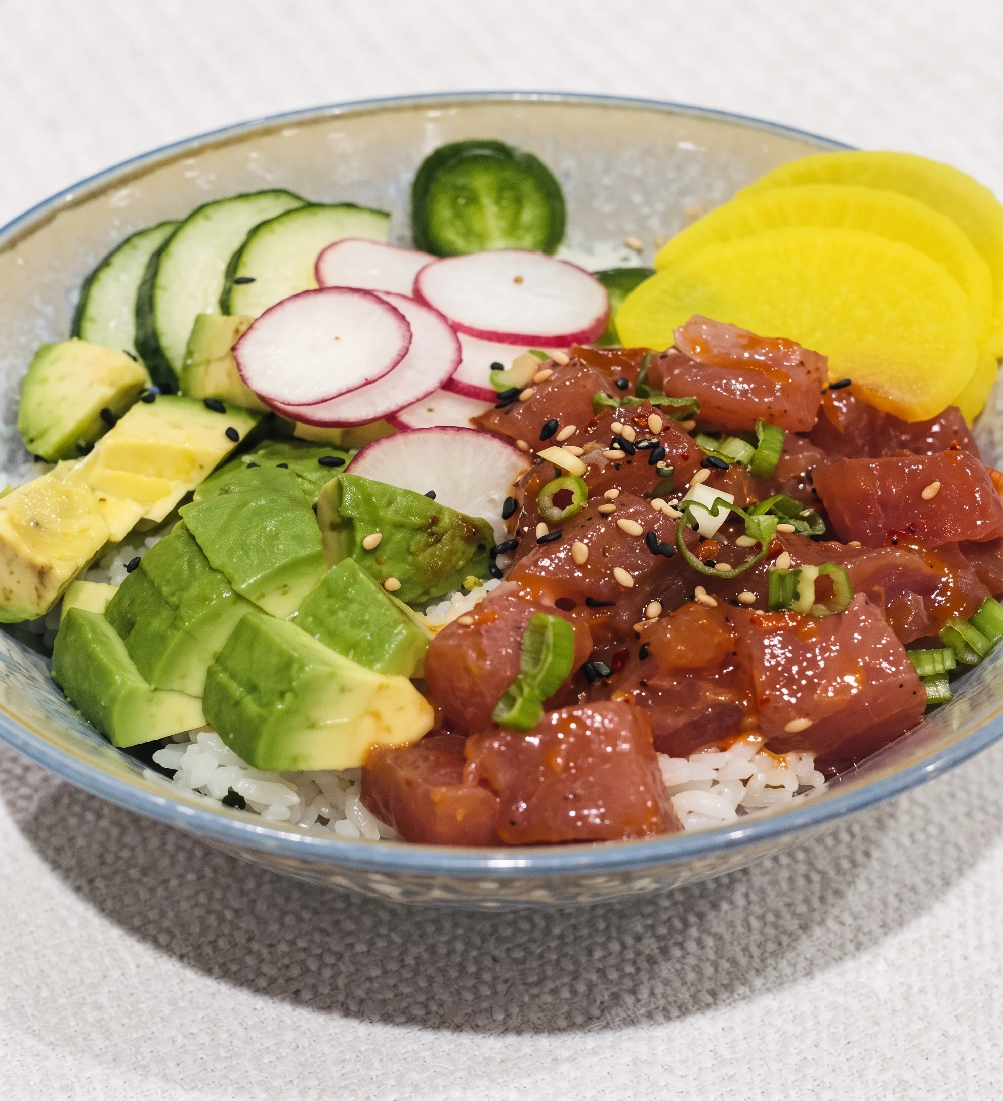 A colorful poke bowl with tuna, avocado, cucumber, and radish on rice.