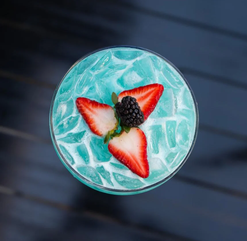 Vibrant blue cocktail garnished with strawberries and blackberries