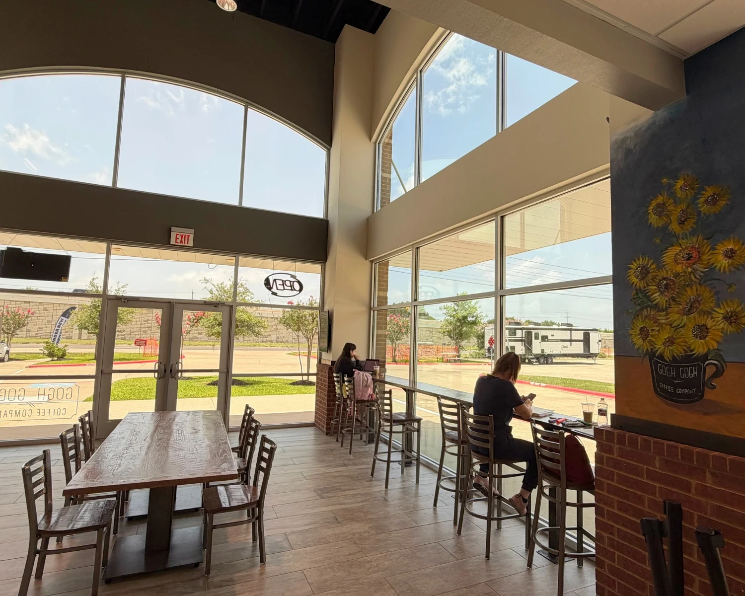 Bright coffee shop interior with large windows and rustic wooden tables