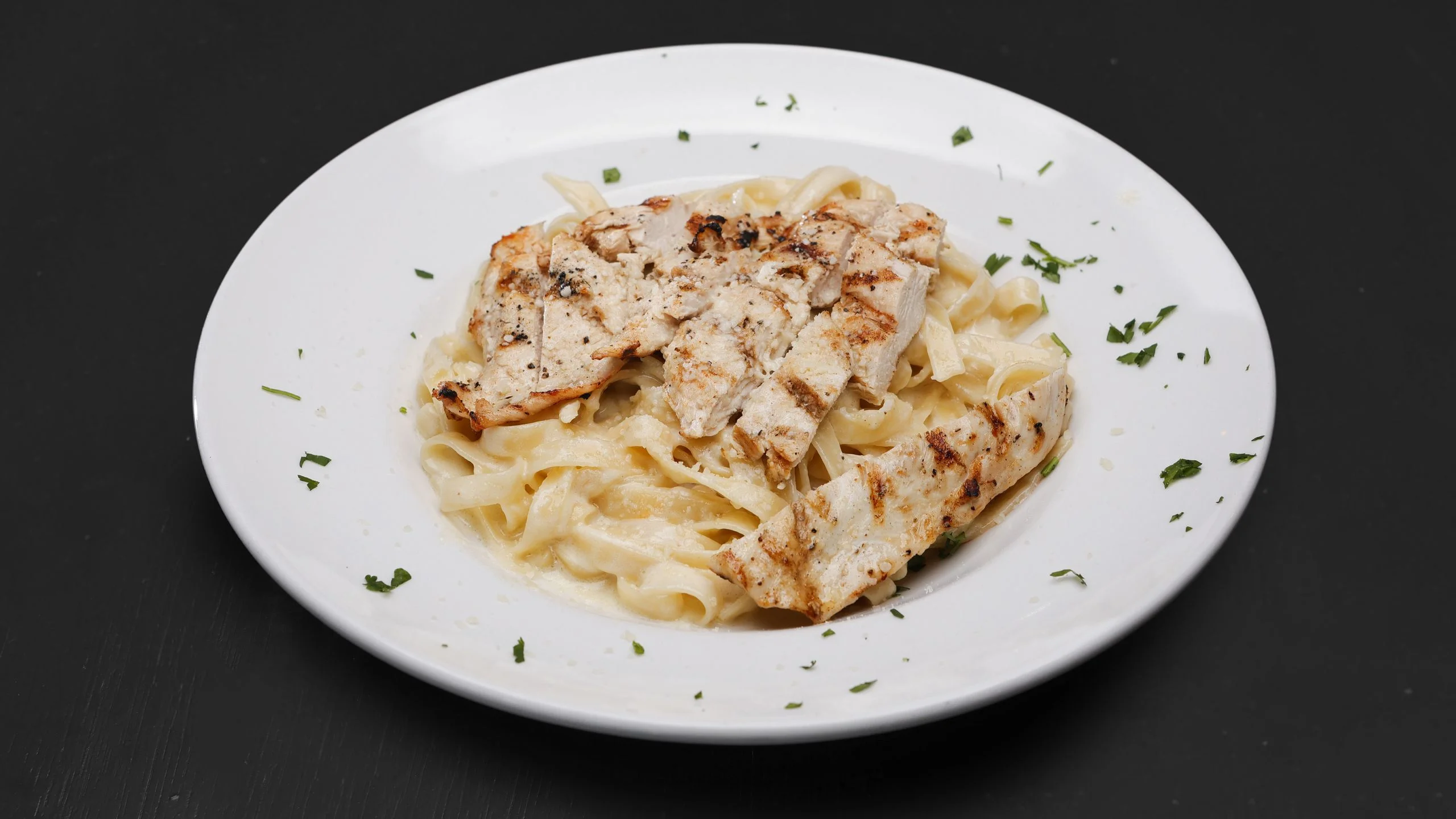 Grilled chicken fettuccine Alfredo on a white plate