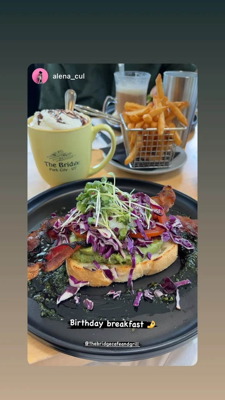 A savory breakfast plate featuring avocado toast topped with bacon, red cabbage, and vegetables, accompanied by fries and a hot beverage.