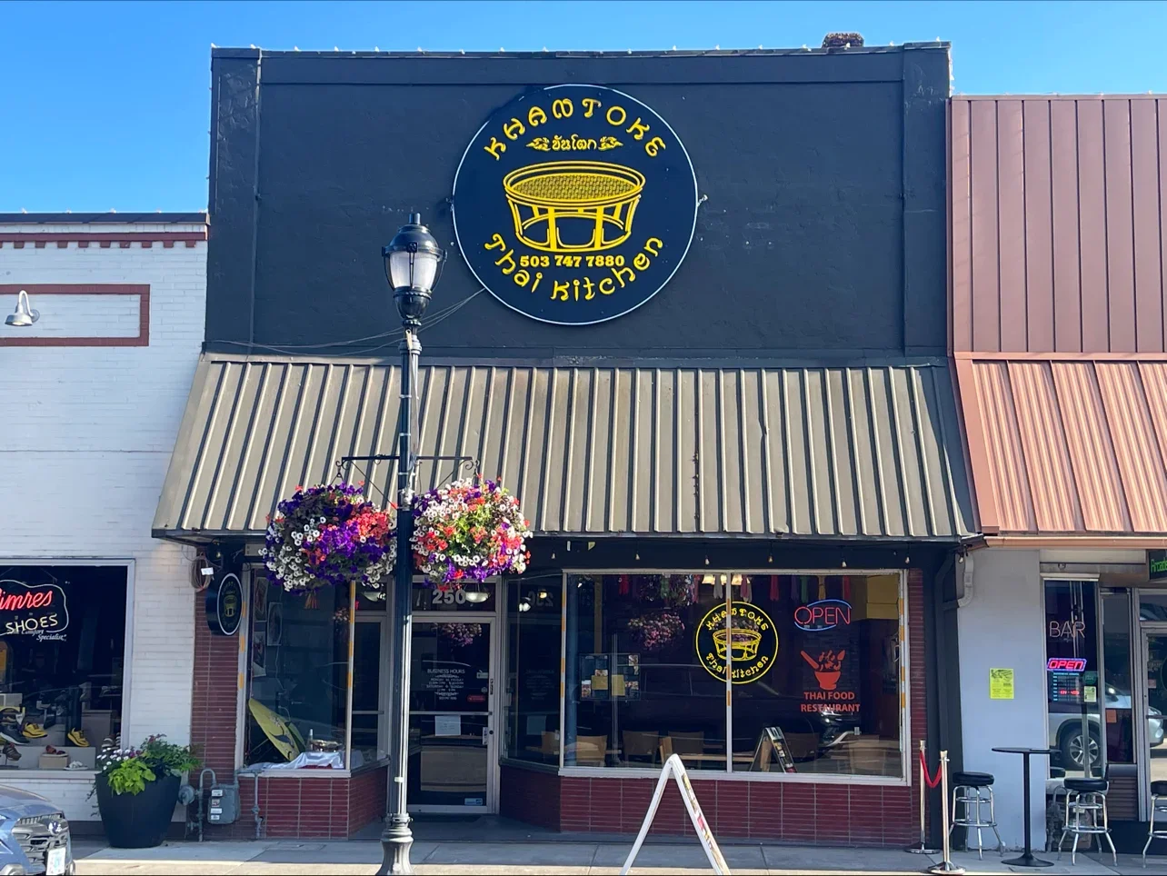 Exterior view of a Thai restaurant with vibrant signage and flower baskets
