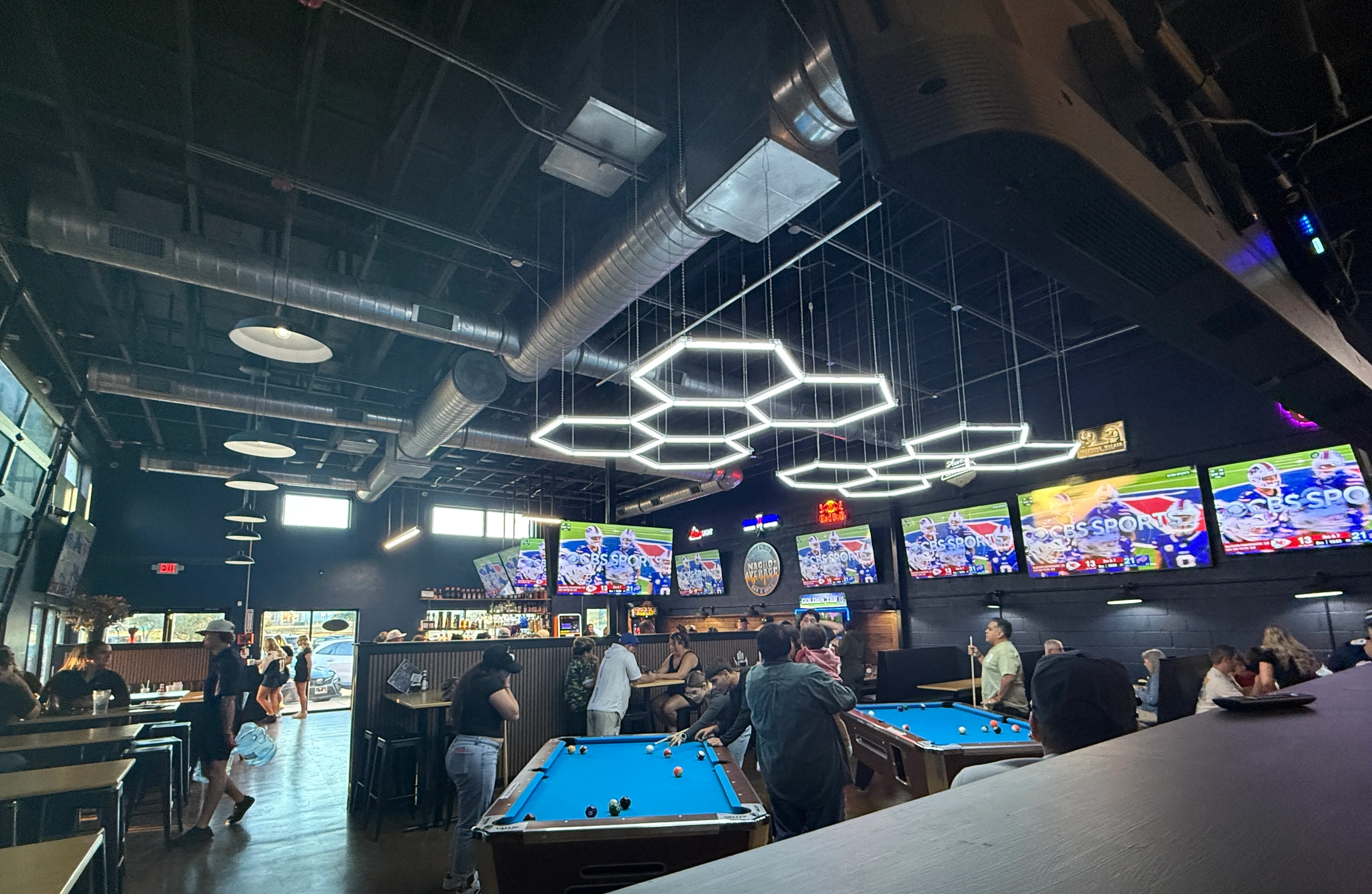 Modern bar interior with pool tables and multiple TVs showing sports
