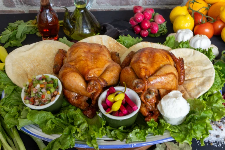Two roasted chickens served with pita and fresh toppings