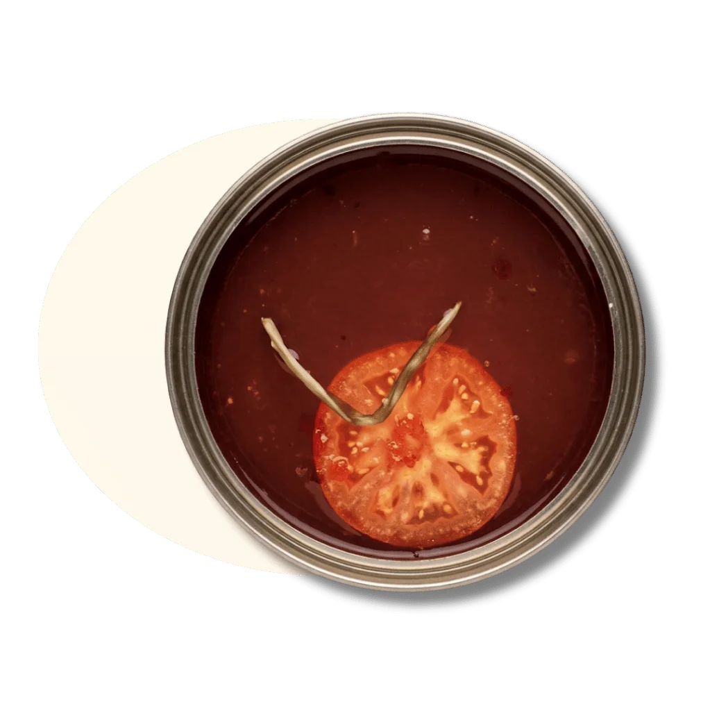 A jar of tomato soup with a slice of tomato and herbs on top.