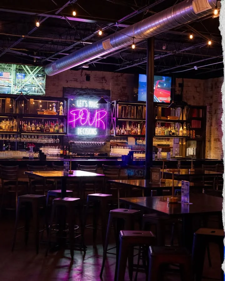 A stylish bar interior with a neon sign and rows of liquor bottles, creating a vibrant atmosphere.