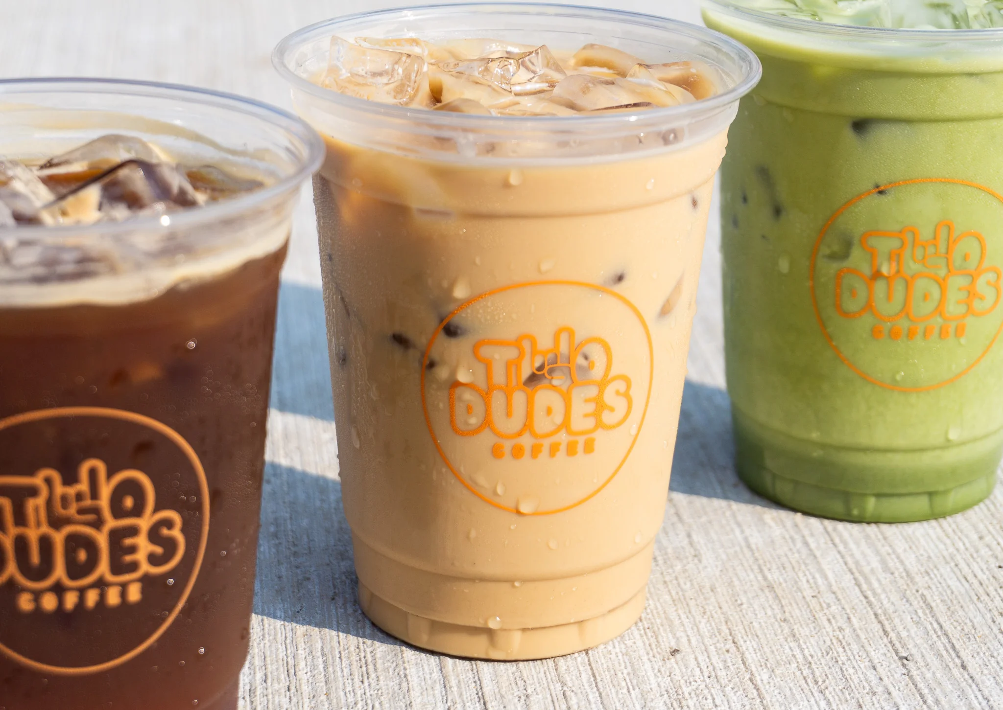 Trio of iced coffee drinks and matcha latte in branded cups