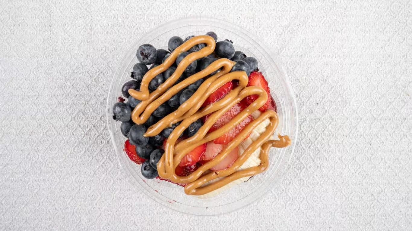 A hand holding a fruit bowl topped with chocolate drizzle, shredded coconut, and an assortment of berries and bananas.