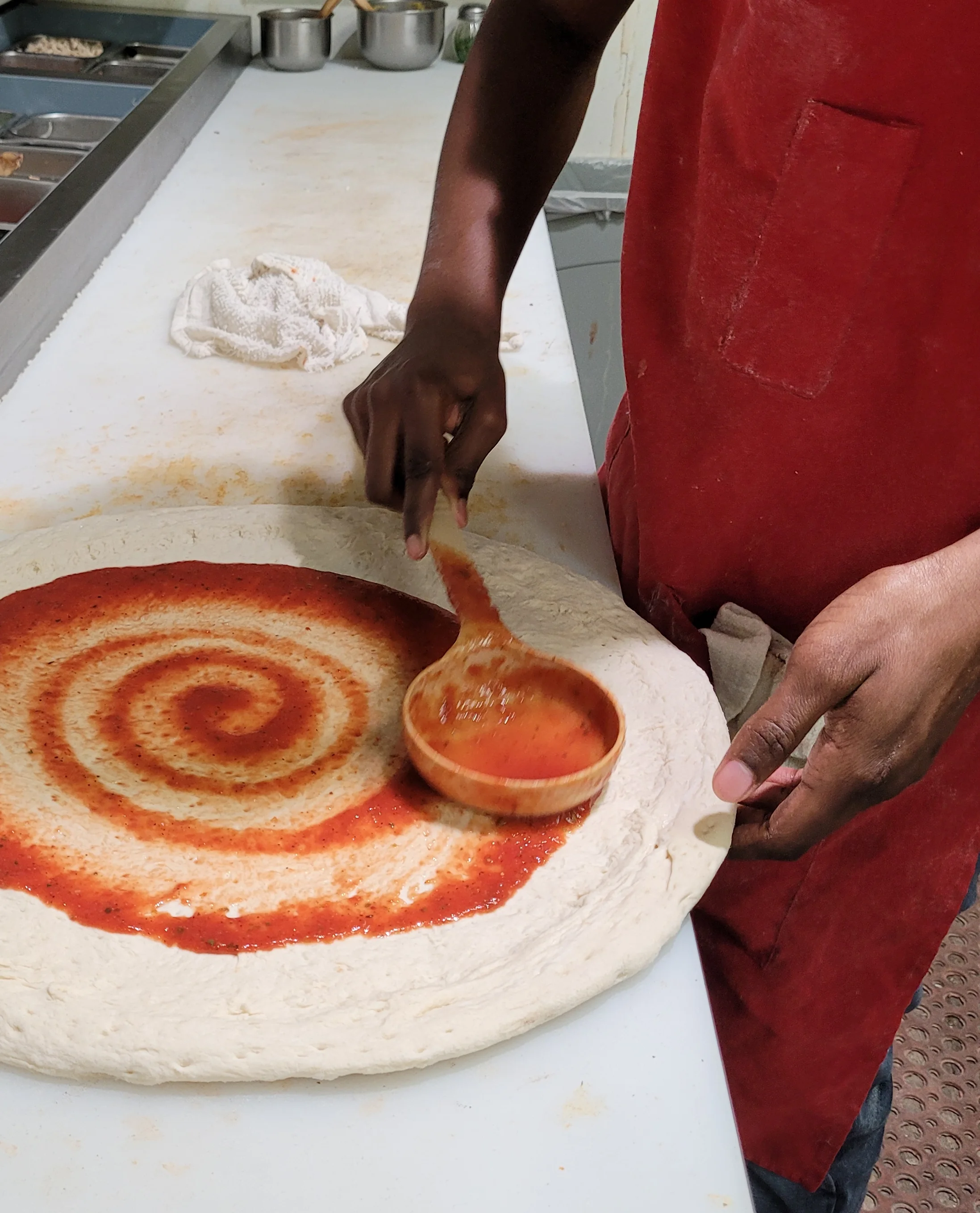 Pizza dough being prepared with tomato sauce in a pizzeria