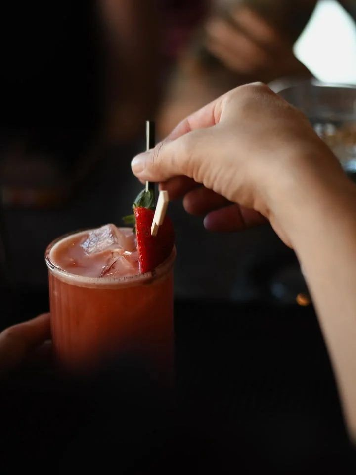 A refreshing cocktail garnished with a strawberry and mint on a stick, filled with ice.