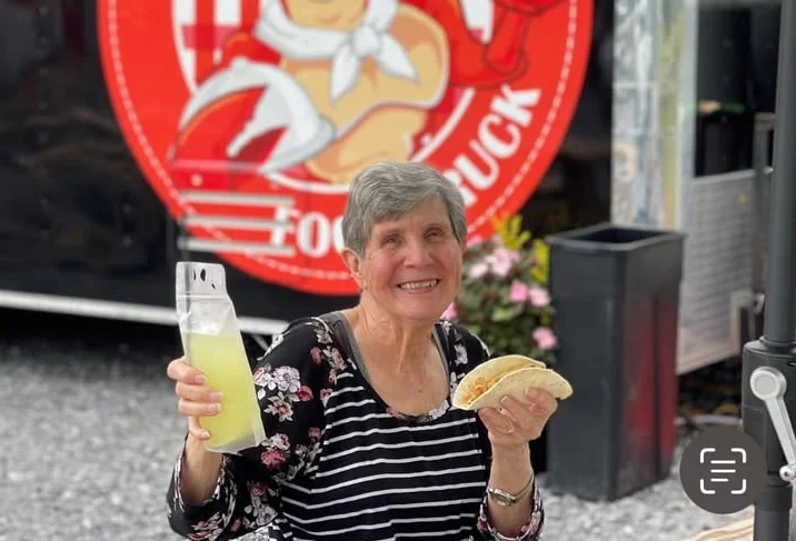 Smiling woman holding a taco and drink at a food truck