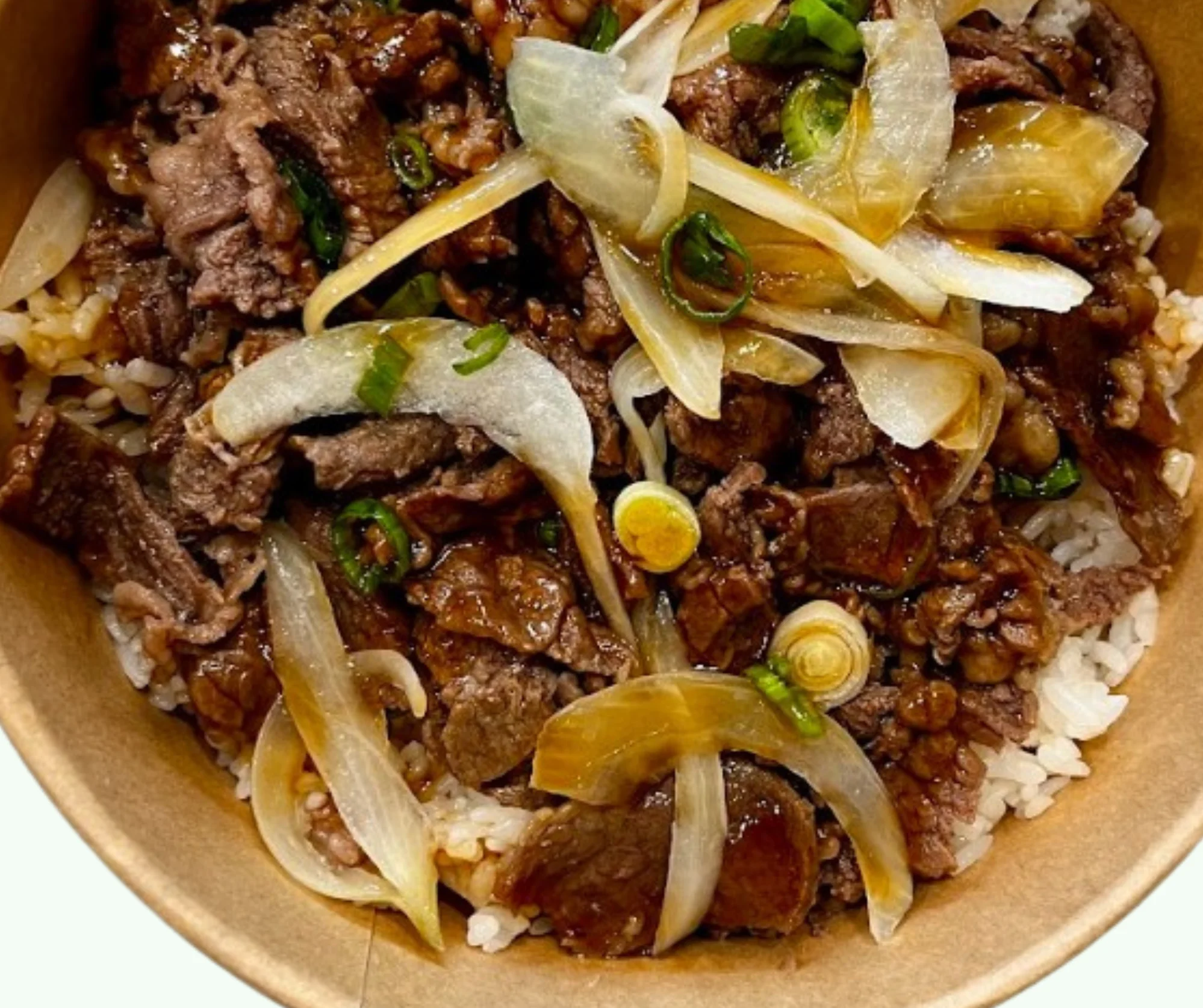 A bowl filled with beef, cooked to a rich brown color, served over a bed of rice and topped with sliced onions and green onions.