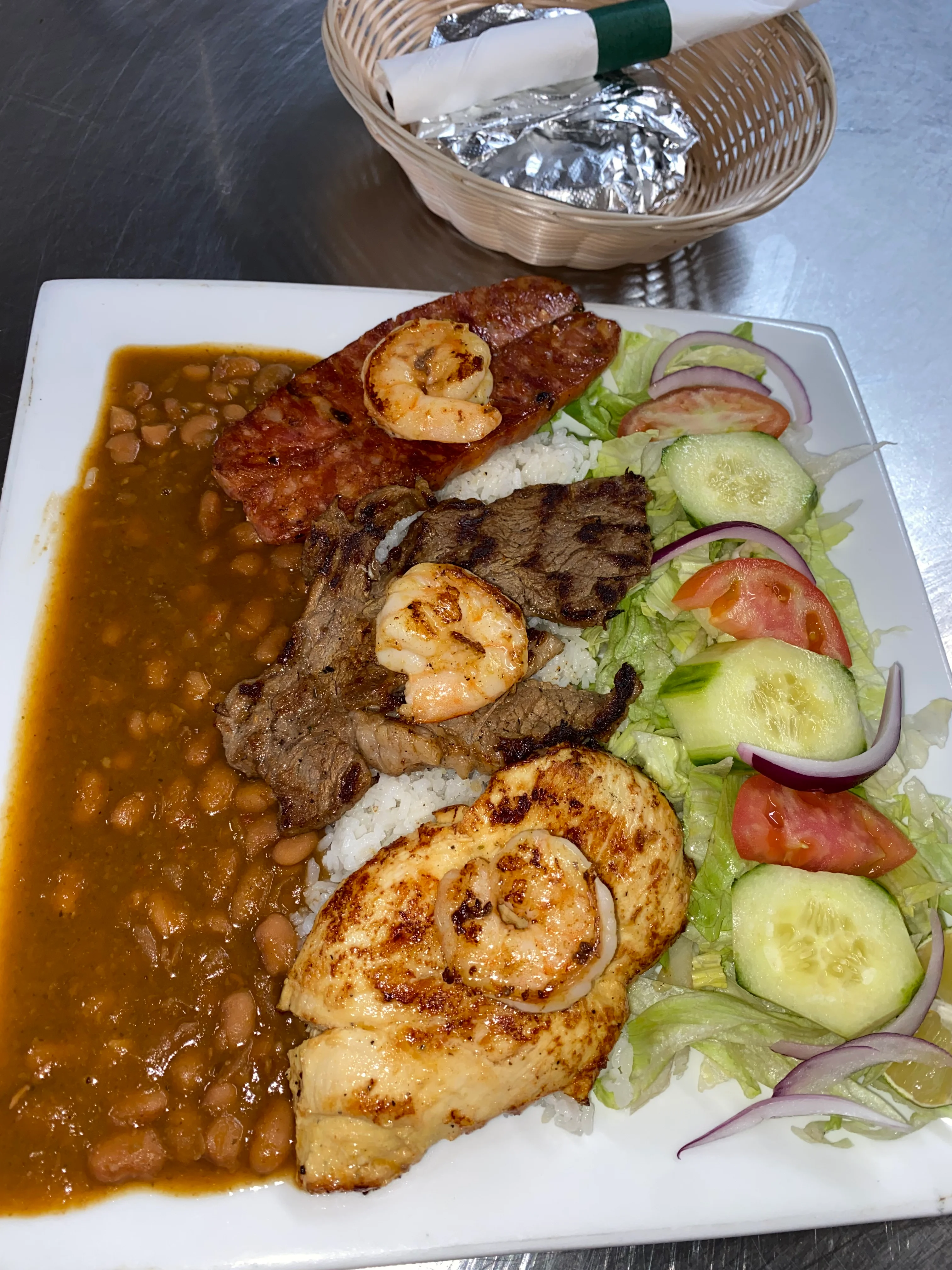 A colorful plate featuring grilled shrimp, assorted meats, rice, beans, and fresh vegetables garnished with a side salad.