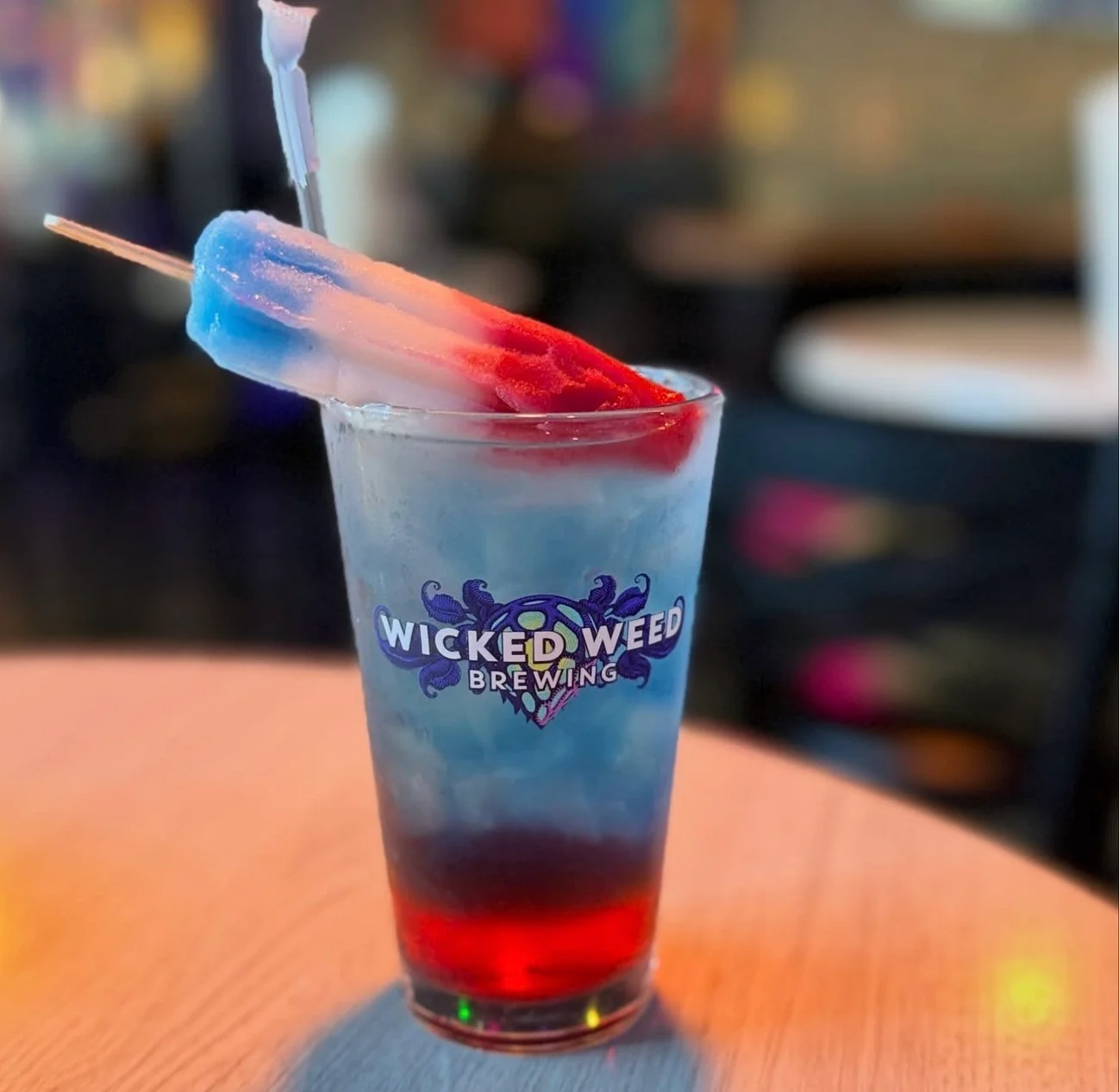 Colorful layered cocktail with popsicle garnish in a branded glass