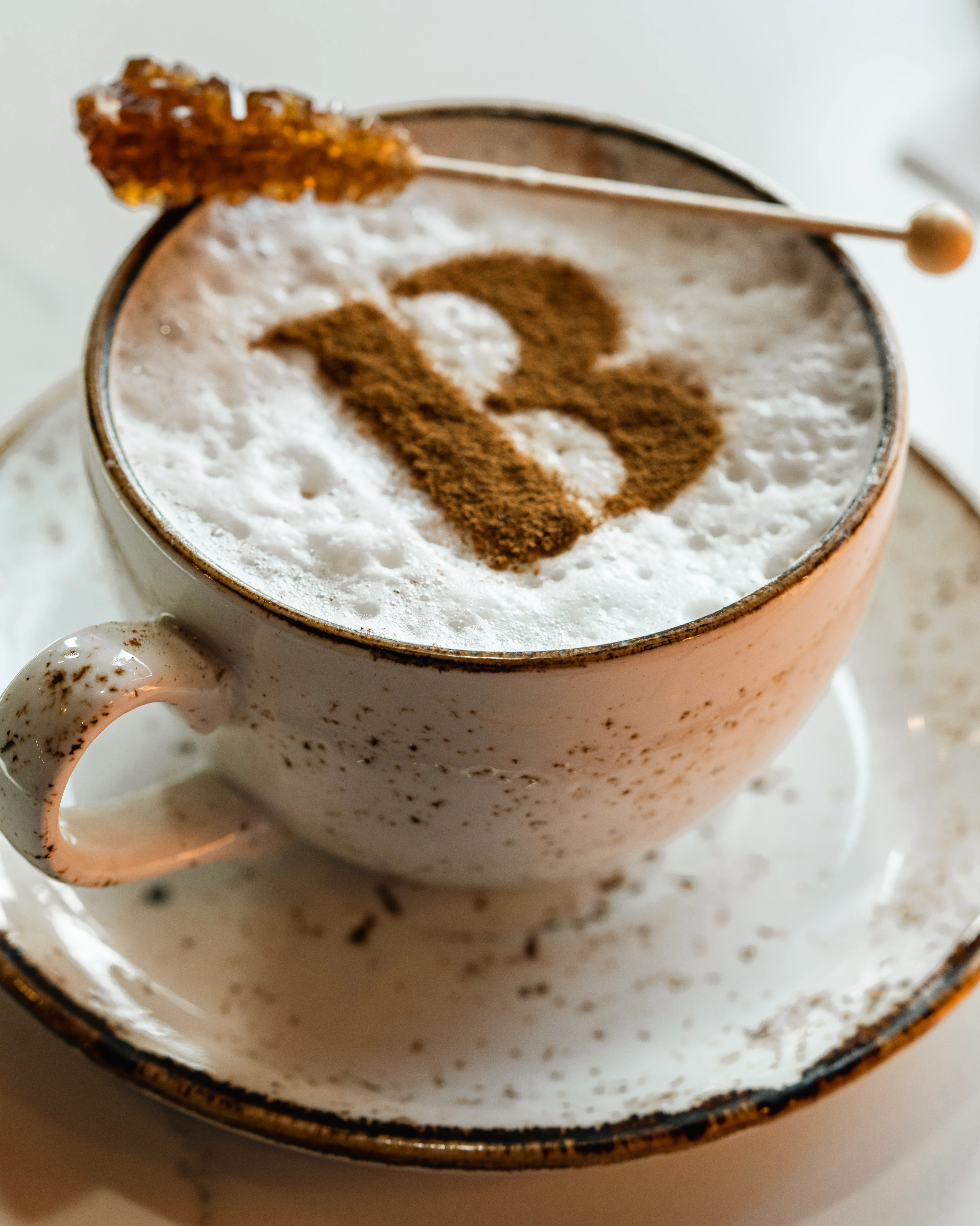 Cappuccino with artistic foam design and honey stick