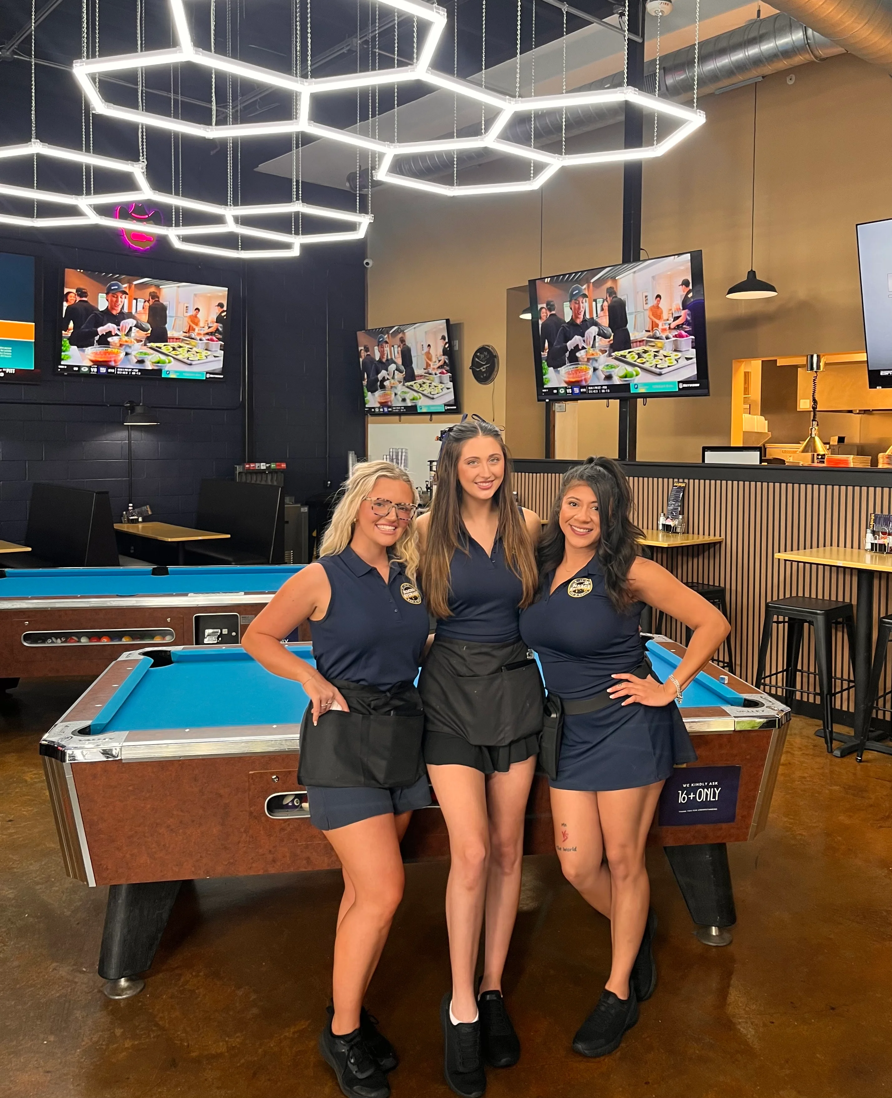 Three staff members posing in a modern bar with pool tables