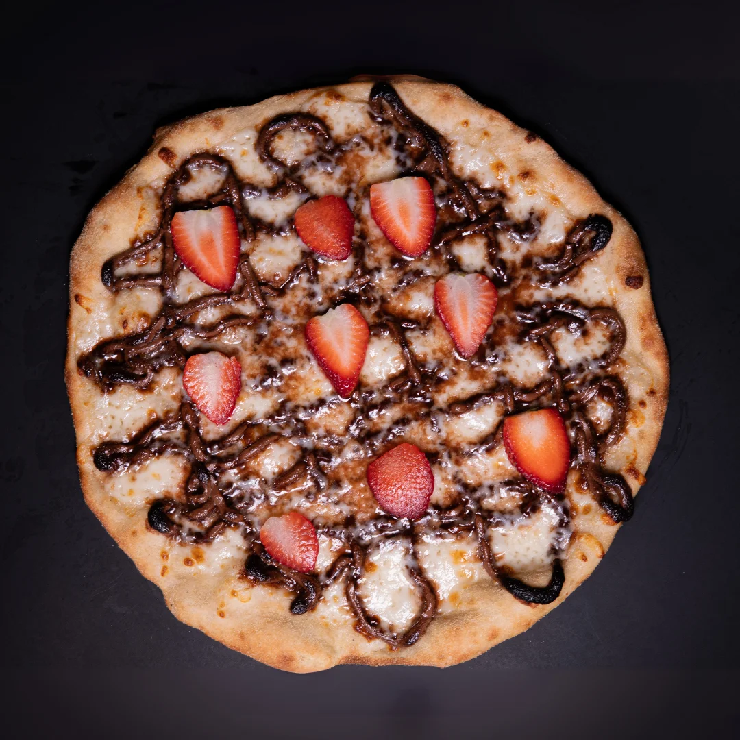 Dessert pizza topped with strawberries and chocolate drizzle